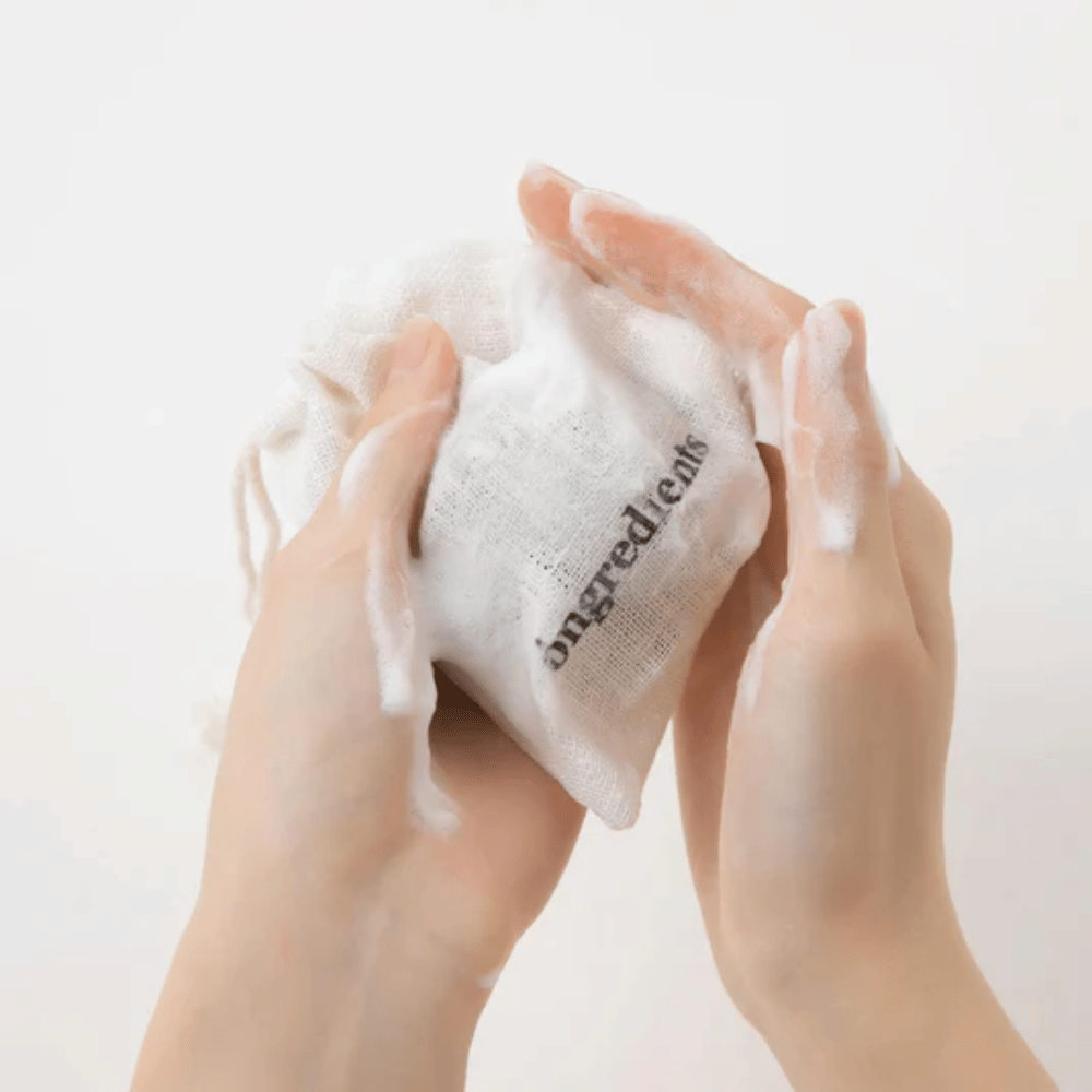 Händer som löddrar upp Óngredients Jeju Green Tea Cleansing Ball i tygpåse – vegansk ansiktsrengöring med grönt te.