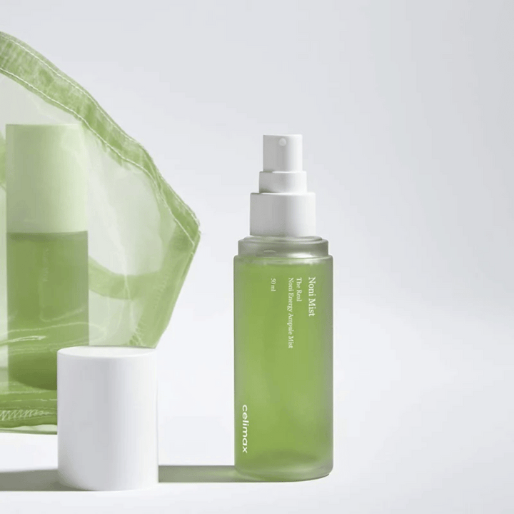 En flaska med Celimax Noni Mist, en grön sprutflaska med vit pump, som står bredvid ett lock. Produkten är förpackad i en genomskinlig plastpåse och marknadsförs som Noni Energy Ampule Mist.