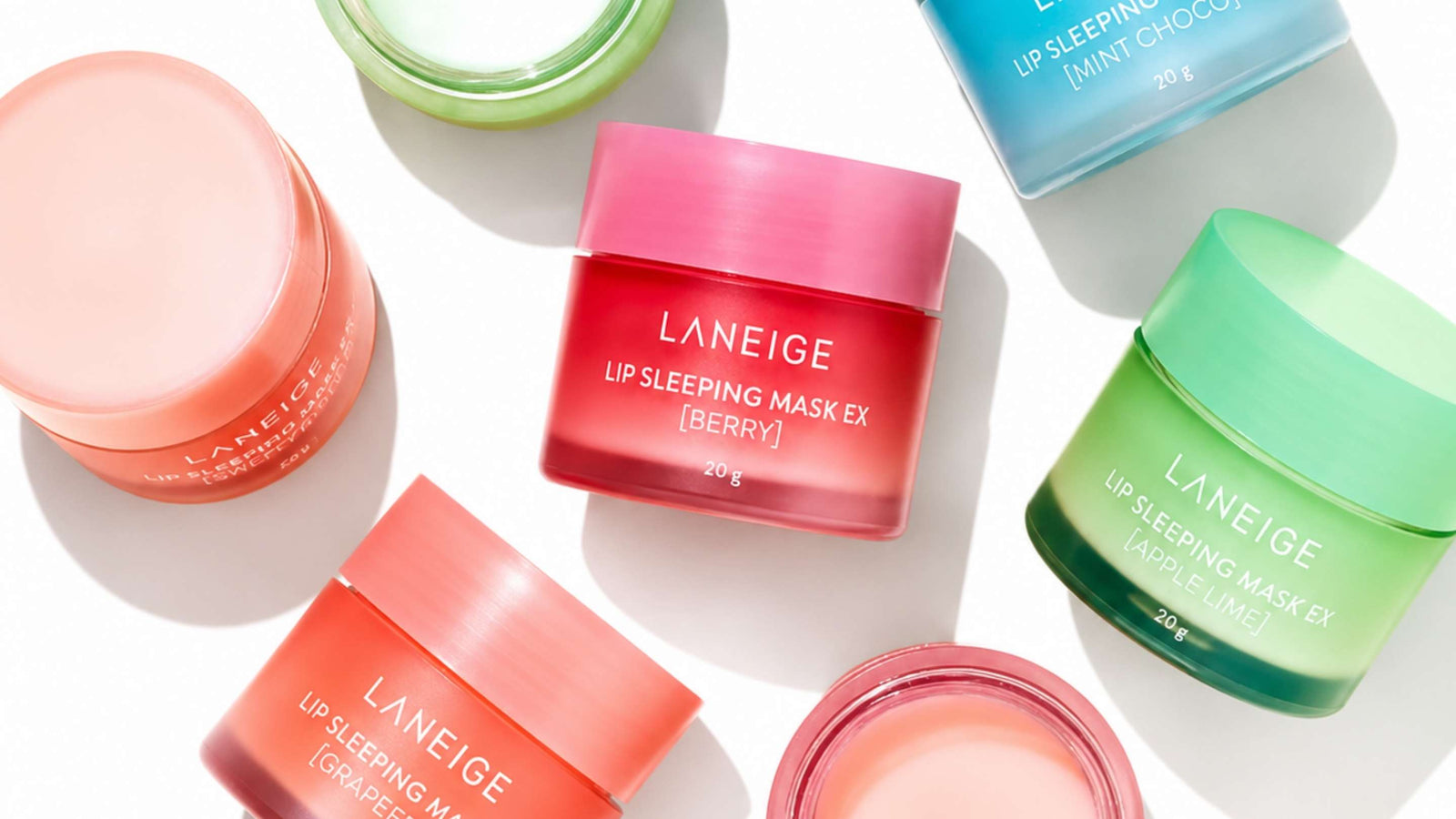 Bilden visar Laneige Lip Sleeping Mask i mango och bärsmaker, omgivna av färska frukter som mango, hallon och blåbär. Produkterna framstår som fuktgivande och näringsrika för läpparna, perfekta för nattvård.