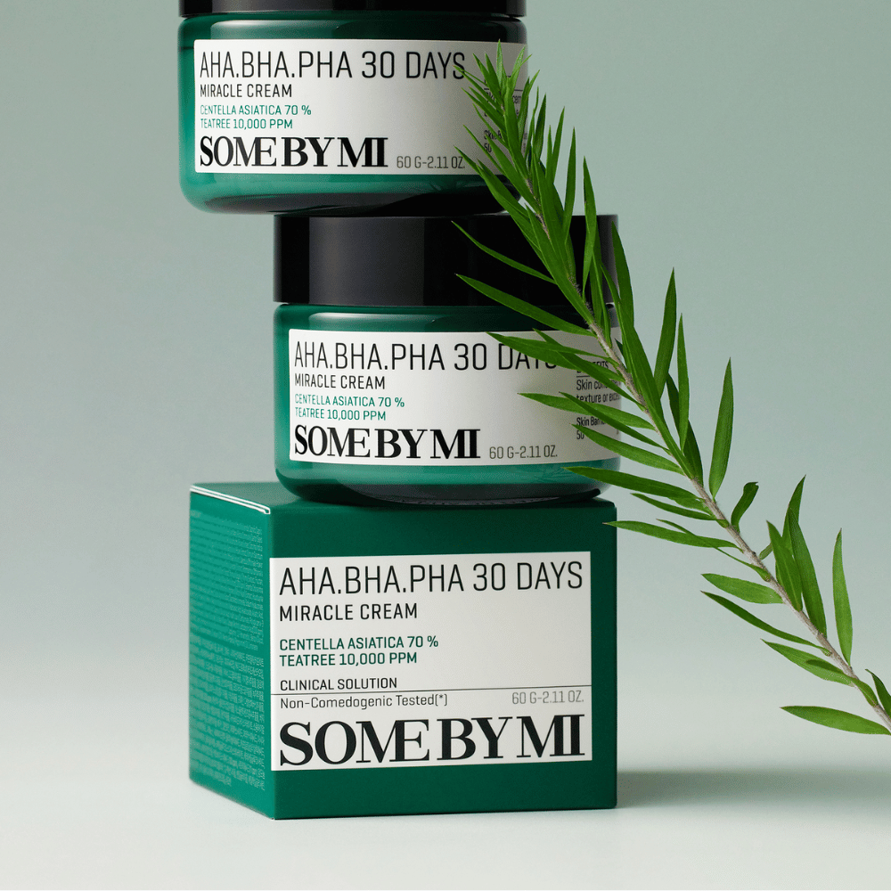 Kuva, joka näyttää kaksi purkkia "SOME BY MI AHA, BHA, PHA 30 Days Miracle Cream" pinottuna vihreäsävyiselle laatikolle. Voide, joka on rikas centella asiaticassa ja tea tree-öljyssä, on suunniteltu parantamaan ihon laatua ja lievittämään ongelmaihoa. Toimii kosteuttavasti ja rauhoittavasti.