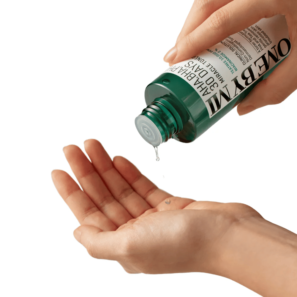 Käsi pitää vihreää pulloa, jossa on teksti "AHA, BHA, PHA 30 Days Miracle Toner" ja puristaa kirkasta nestettä toisen käden kämmenelle, valmiina käyttöön.