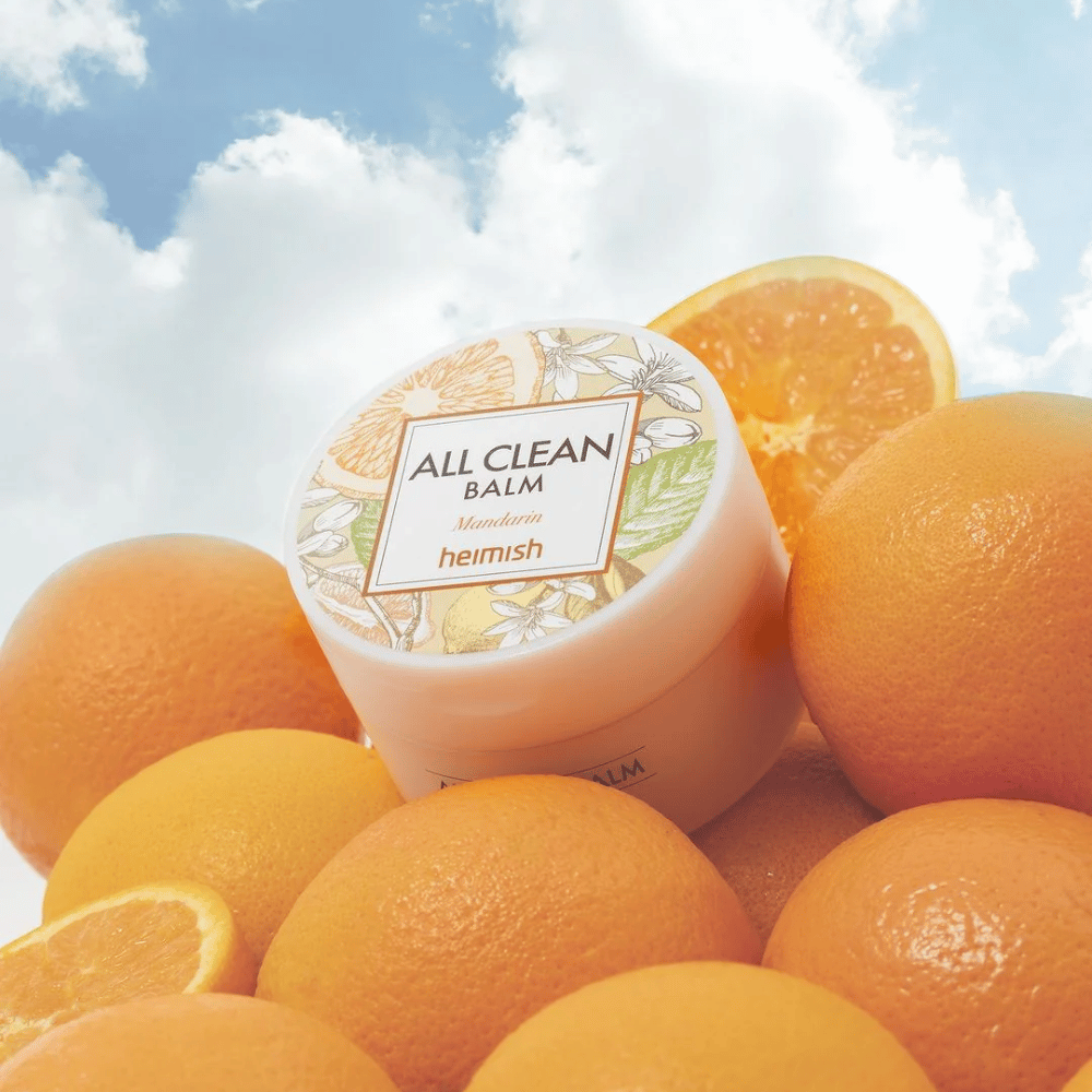 Purkki Heimish All Clean Balm Mandarin sijoitettuna appelsiinikasaan, sininen taivas taustalla.