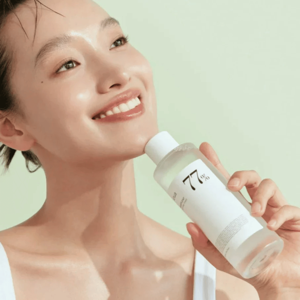 Nainen rauhoittaa herkkää ihoaan pullolla Heartleaf 77% Soothing Toner Anua, joka sisältää kameleonttilehtiuutetta.