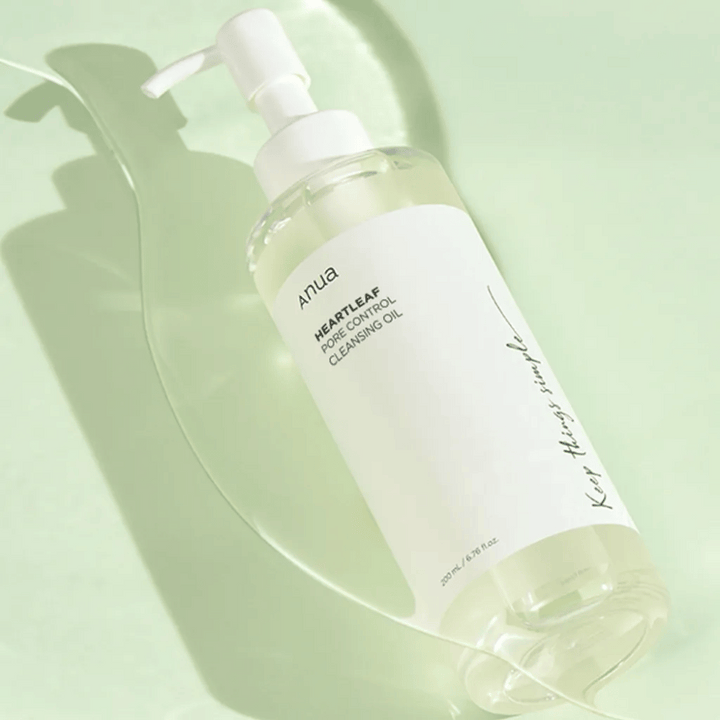 På bilden syns ANUA Heartleaf Pore Control Cleansing Oil, en rengöringsolja med pumpdesign. Flaskan är genomskinlig och innehållet ser ut att vara av en lätt, oljig konsistens. Etiketten bär varumärkets logotyp och produktnamn i enkel och stilren text, vilket bidrar till en känsla av minimalistisk skönhet och renhet. Det står "Keep things simple" som en del av designen, vilket antyder en filosofi om enkelhet i hudvårdsrutinen. Flaskan innehåller 200 ml produkt.