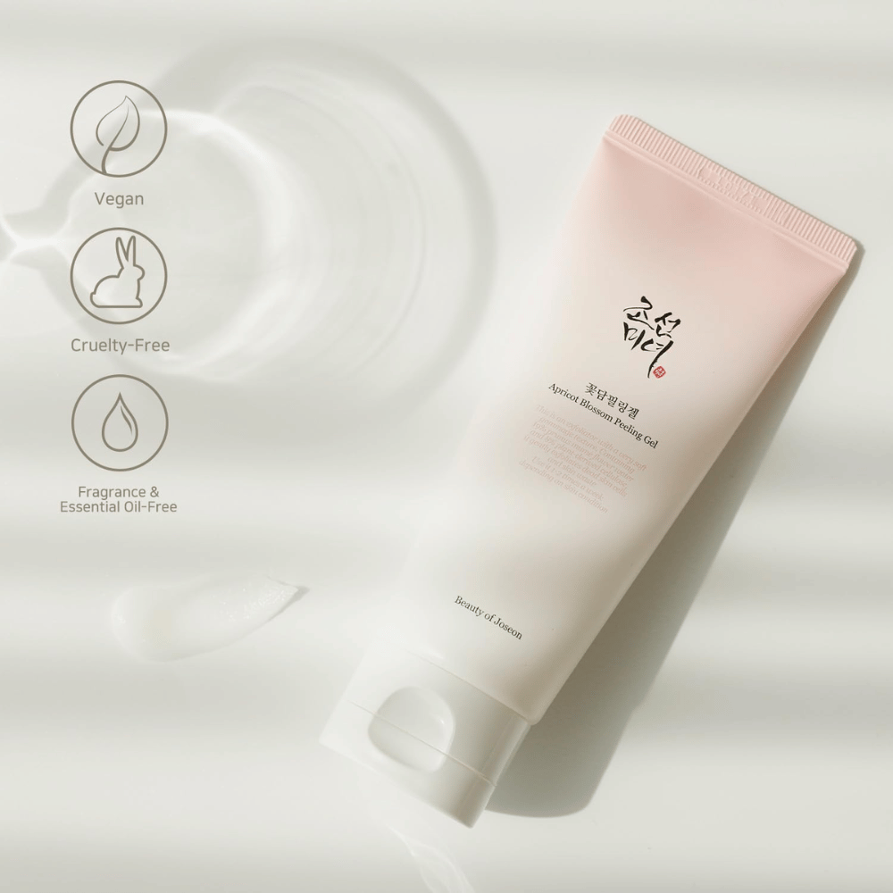 Putki, jossa on Apricot Blossom Peeling Gel, makaa heijastavalla pinnalla ikonien kanssa, jotka osoittavat, että tuote on vegaaninen, eläinystävällinen ja vapaa tuoksuista ja eteerisistä öljyistä.