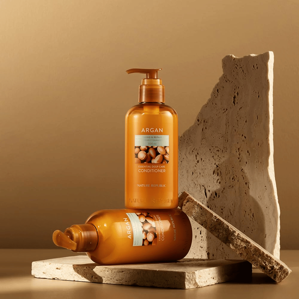 Kaksi pulloa Nature Republic Argan Essential Moisture Repairing Conditioner kivipinnalla lämpimässä sävyssä.