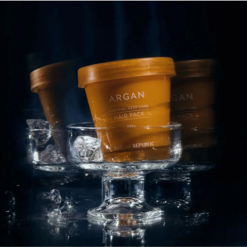 Nature Republic Argan Essential Moisture Repairing Hair Mask sijoitettu lasilautaselle jääpalojen kanssa – ylellinen ja hoitava hiusnaamio.