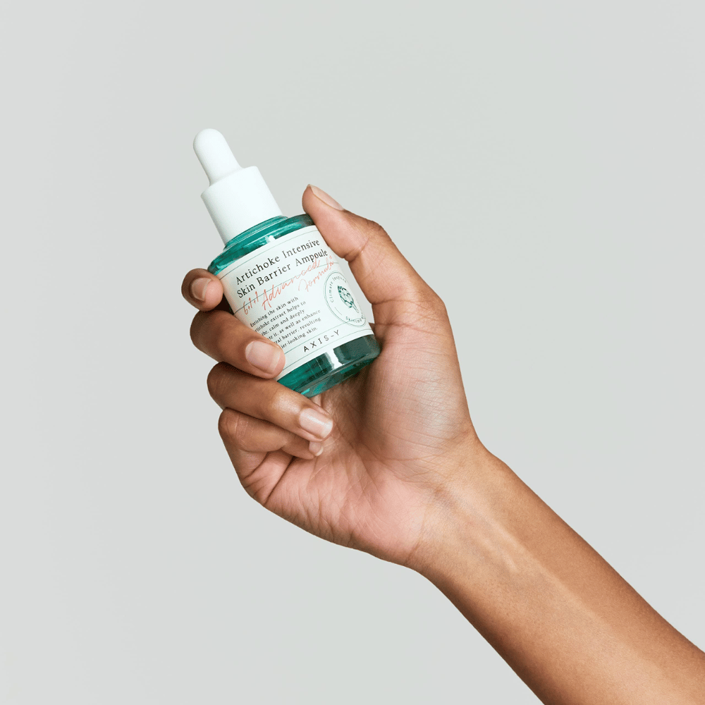 Käsi pitelee ihonhoitoseerumipulloa, jossa on etiketti "Artichoke Intensive Skin Barrier Ampoule.