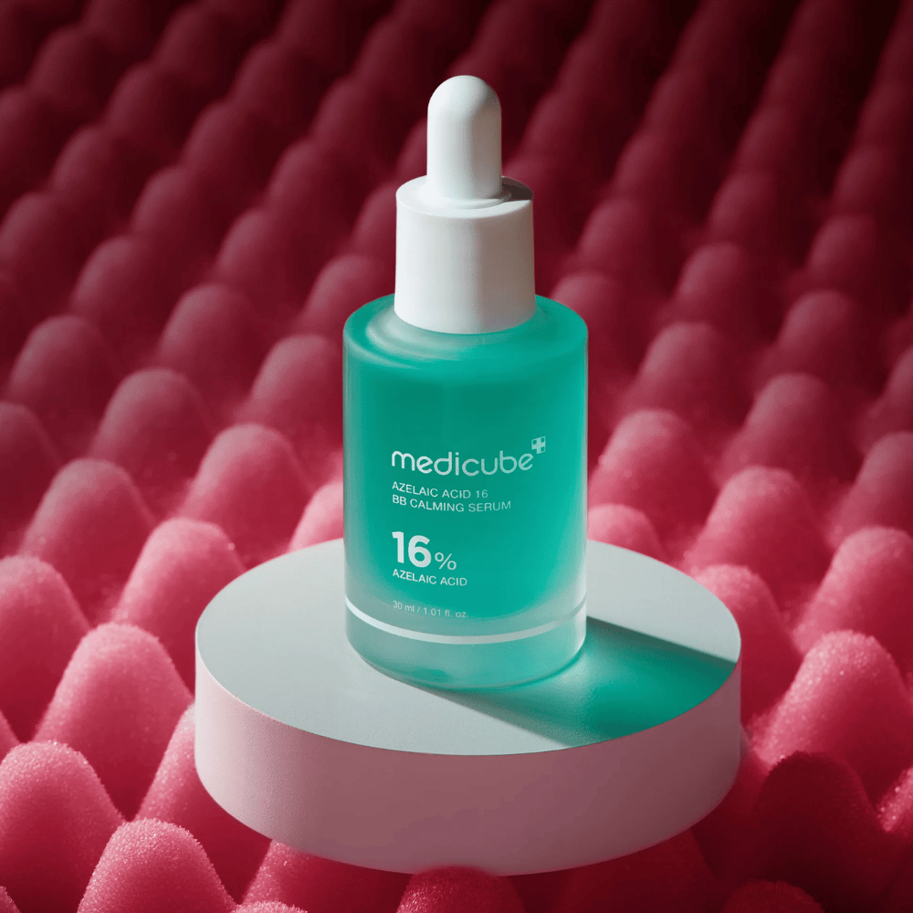 Tuotekuva tuotteesta Medicube Azelaic Acid 16 BB Calming Serum, asetettuna valkoiselle podium-alustalle vaaleanpunaisen teksturoidun taustan eteen, mikä korostaa seerumin rauhoittavaa ja ihoa parantavaa profiilia.