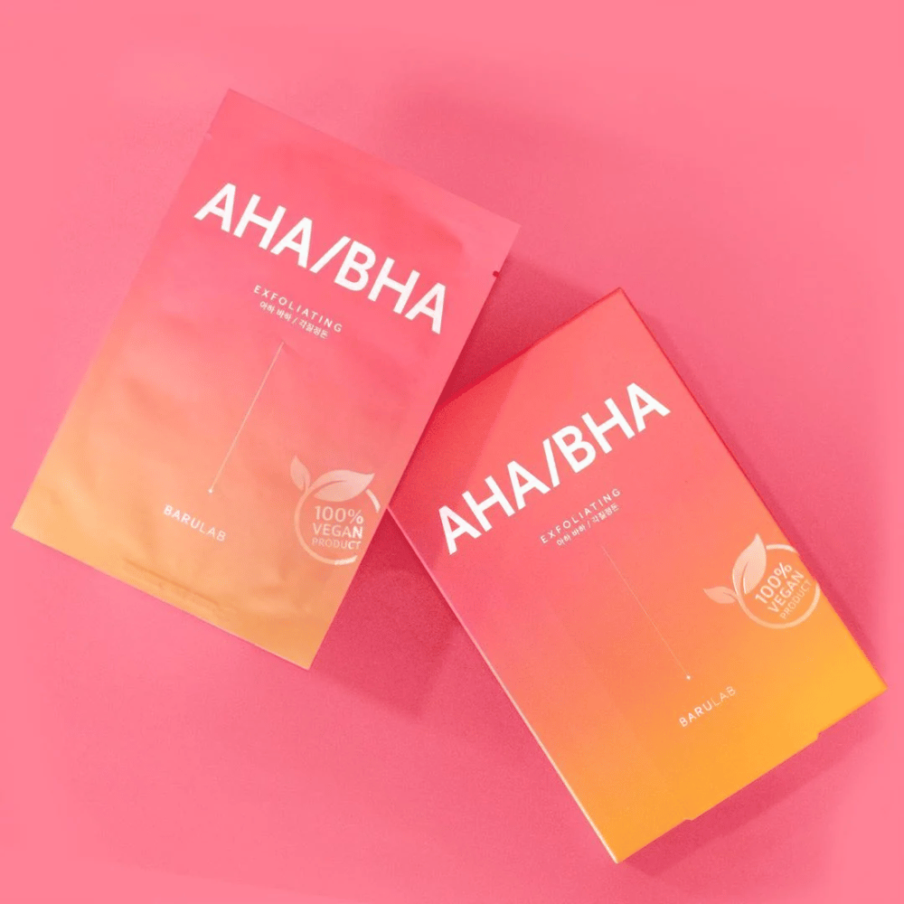 Kaksi tuotetta BARULAB, yksi pussissa ja yksi laatikossa, molemmat merkitty "AHA/BHA" ja "Exfoliating" vaaleanpunaisella taustalla. Tuotteet on merkitty "100% Vegan Product".