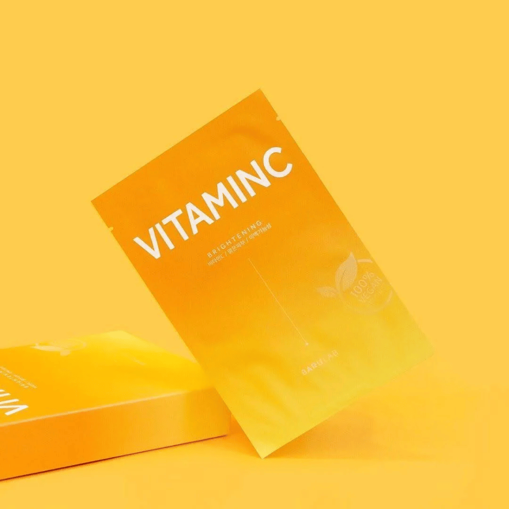 Pino pakkauksia BARULAB "VITAMINC Brightening" -naamioista, kaikki merkitty "100% Vegan Product". Pakkauksissa on värisävyjä eri oranssin ja keltaisen sävyissä, asetettu yhtenäiselle keltaiselle taustalle.