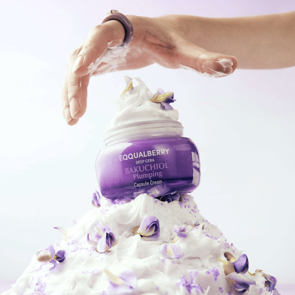 EQQUALBERRY Bakuchiol Plumping Capsule Cream sijoitettuna kermavaahdon päälle, jossa on kukkien terälehtiä – symboloi kosteutusta ja hoitoa.