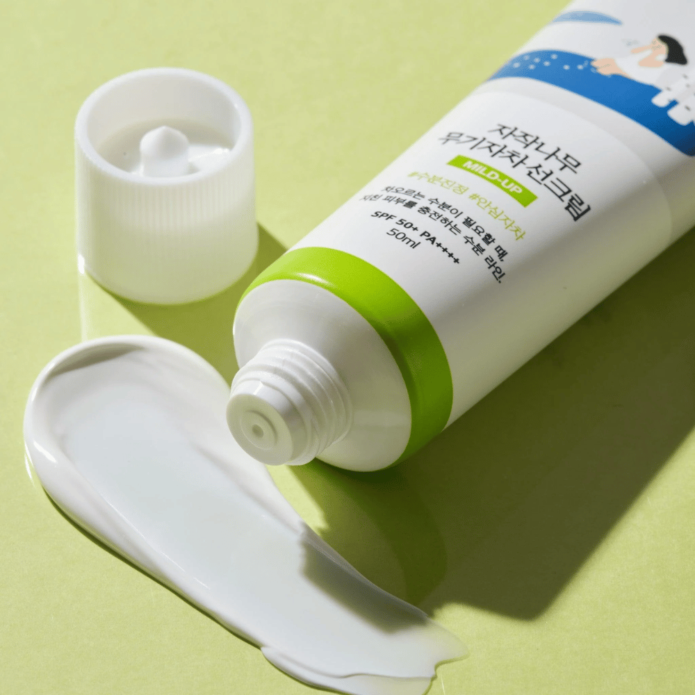 Lähikuva Birch Juice Moisturizing Mild Up Sunscreen avokorkilla, valkoinen aurinkovoide levitettynä vaaleanvihreällä taustalla, SPF 50+ PA++++, 50 ml.