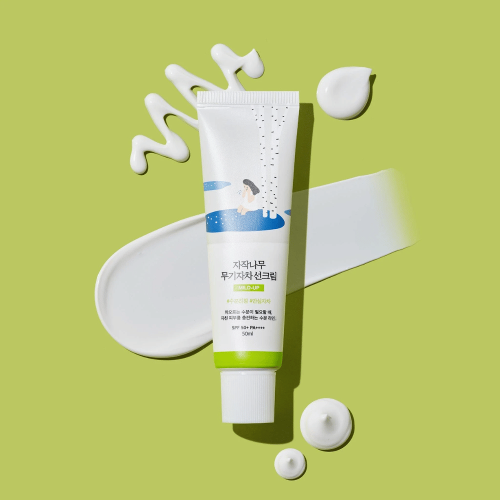 Birch Juice Moisturizing Mild Up Sunscreen – valkoinen tuubi vihreällä pohjalla vihreällä taustalla, ympäröity levitetyllä aurinkovoiteella ja pisaroilla, SPF 50+ PA++++, 50 ml.