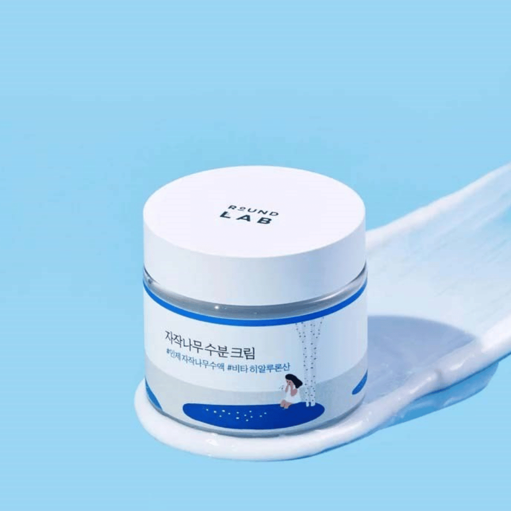 Round Lab Birch Juice Moisturizing Cream sinisävyisessä purkissa, jossa on valkoinen kansi, seisoo kerroksessa kermaa sinistä taustaa vasten.