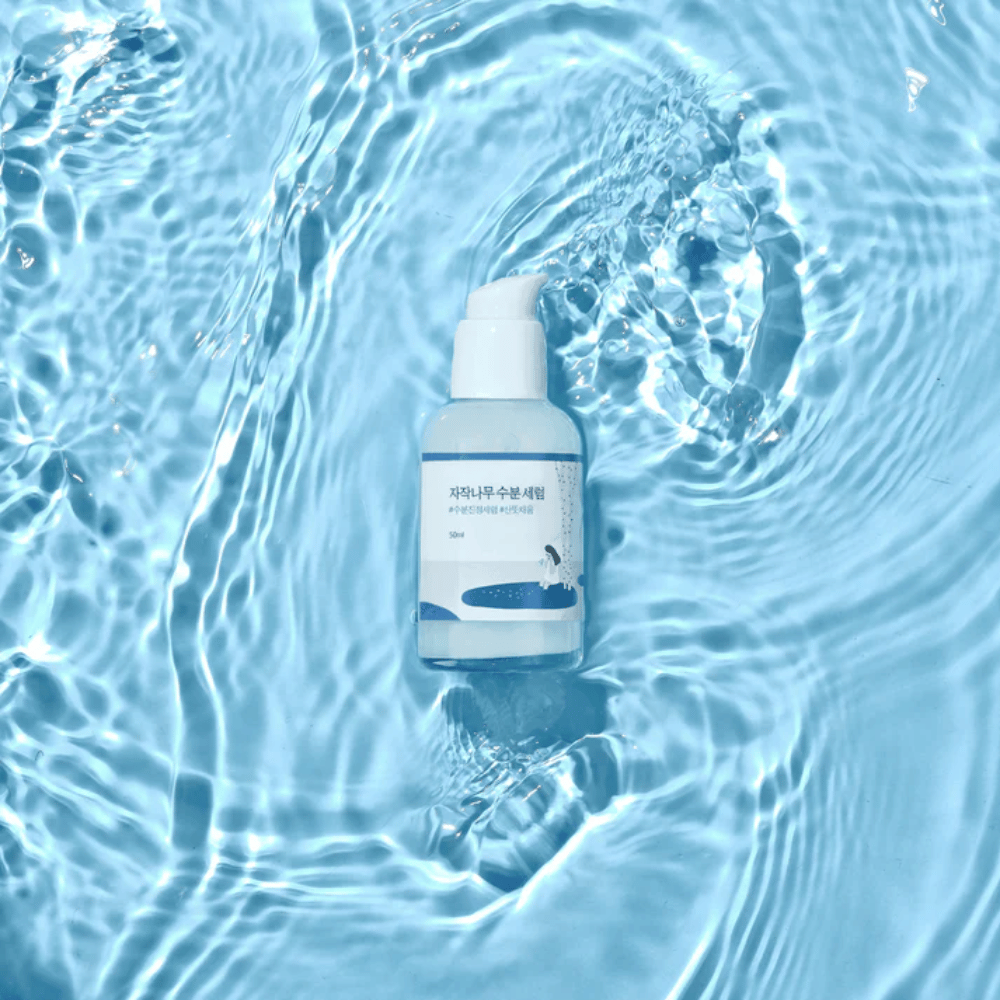 Round Lab Birch Juice Moisturizing Serum pumppupullossa kellumassa sinisen veden päällä auringonvalon heijastuksineen.