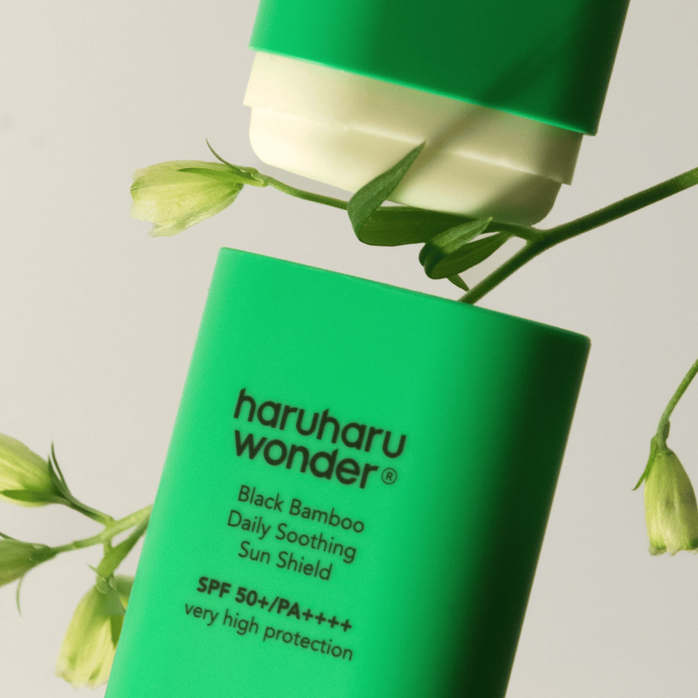 Lähikuva Haruharu Wonder Black Bamboo Daily Soothing Sun Shield – vihreä aurinkosuoja puikkomuodossa SPF 50+ PA++++, ympäröity vihreillä kasvien yksityiskohdilla.