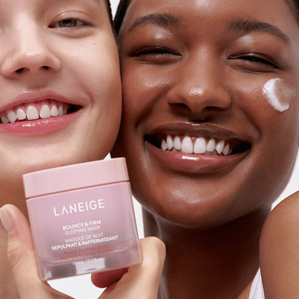 Kaksi henkilöä hymyilee ja pitää kädessään Laneige Bouncy & Firm Sleeping Mask. Toinen on levittänyt naamiota poskelleen, ja tuote näkyy selvästi heidän käsissään. Naamio on vaaleanpunaisessa purkissa ja markkinoidaan nimellä "Täyteläisyys, Kosteutus, Hehku."