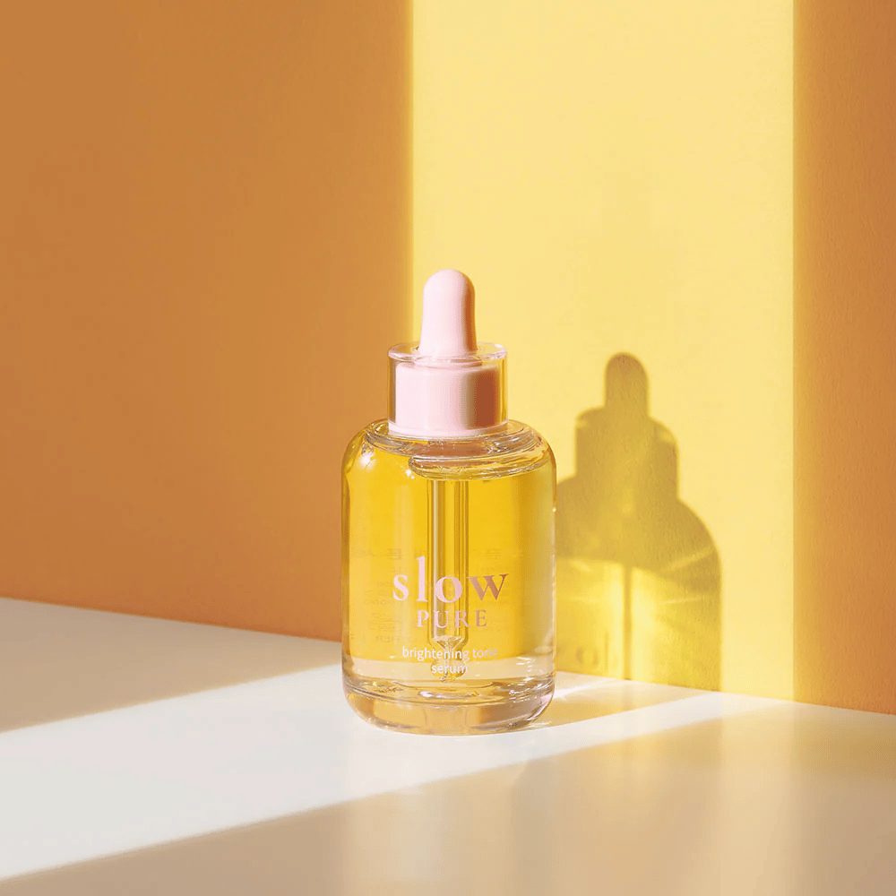 Slow Pure Brightening Tone Serum aurinkoisessa keltaisessa valossa, symboloi hehkua ja energiaa iholle.