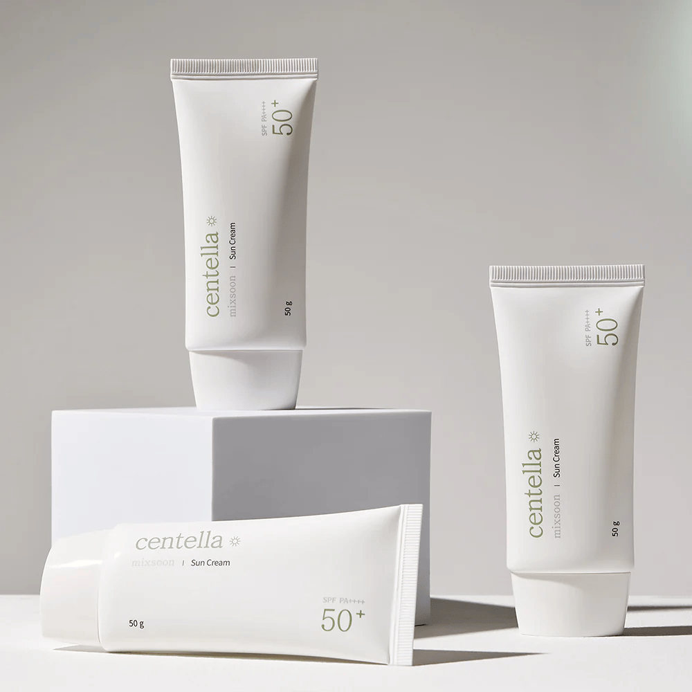 Kolme Centella Sun Cream SPF 50+ PA++++ pakkausta järjestetty esteettisesti valkoisille jalustoille. Kaksi putkiloa seisoo ja yksi makaa, kaikissa on valkoinen, minimalistinen muotoilu ja vihreät tekstiyksityiskohdat.