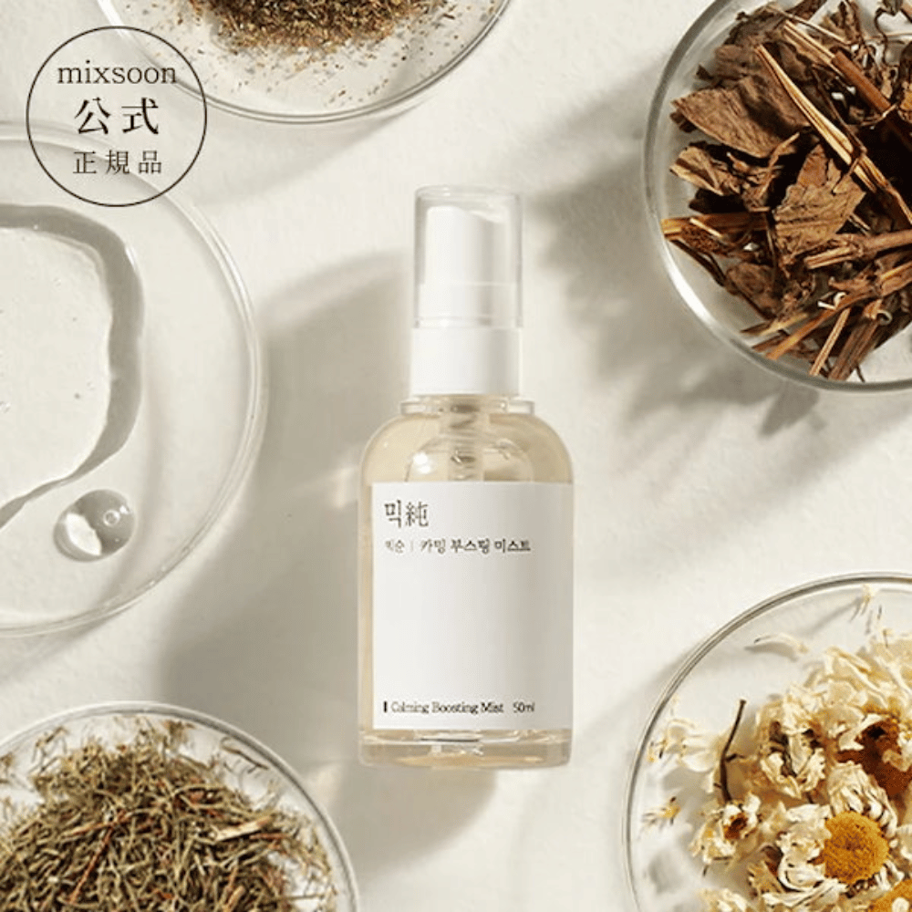 Läpinäkyvä suihkepullo etiketillä 'Calming Boosting Mist' Mixsoon, ympäröity kuivatuilla yrteillä ja kukilla valkoisilla kulhoilla beigeä taustaa vasten, mikä korostaa tuotteiden luonnollisia ainesosia.