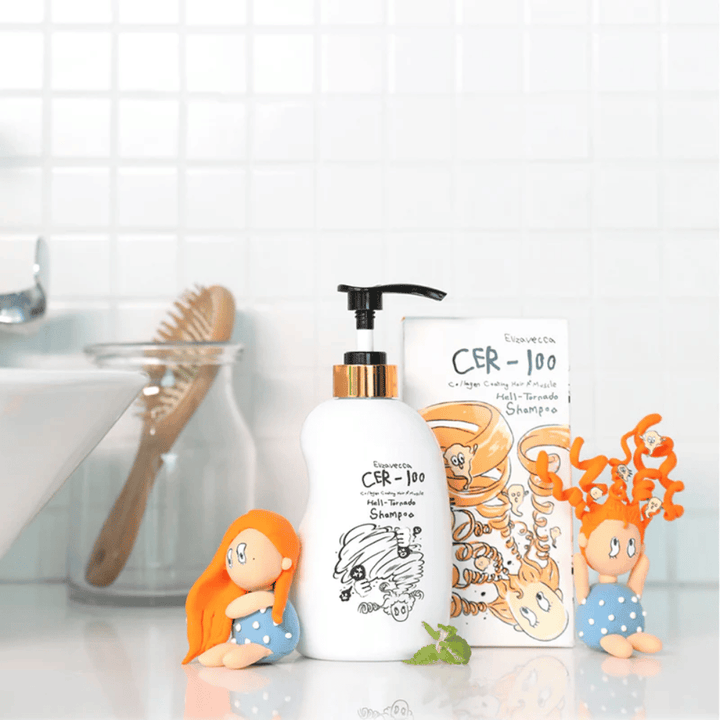 Elizavecca CER-100 Shampoo ja kartonkipakkaus näkyvät kylpyhuoneympäristössä hiusharjan ja koristeellisten hahmojen vieressä. Kuva välittää arkisen hiustenhoitorutiinin ja tuotteen käytön kotiympäristössä.