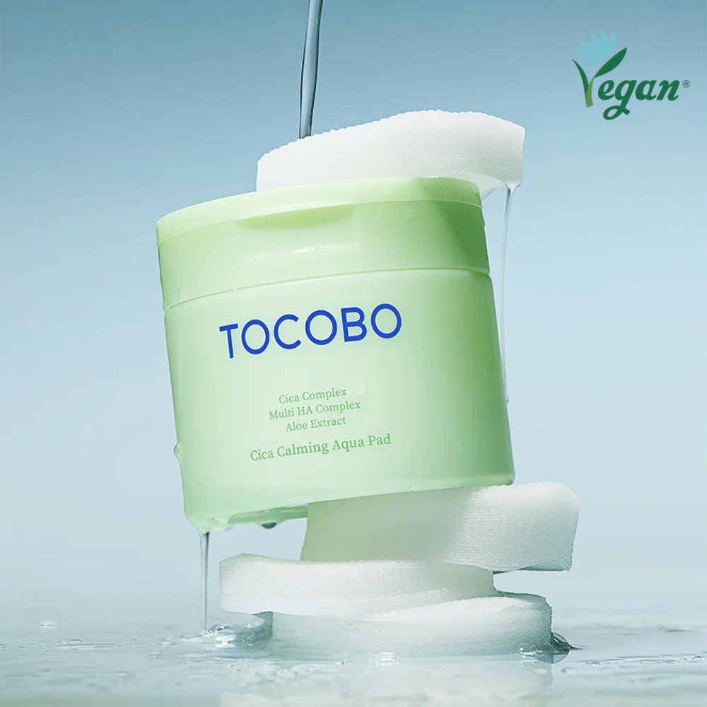 TOCOBO Cica Calming Aqua Pad aseteltuna toner padien väliin valuvan essencen kanssa. Vegaanisymboli korostaa tuotteen vegaanista koostumusta ja ihoystävällistä profiilia.