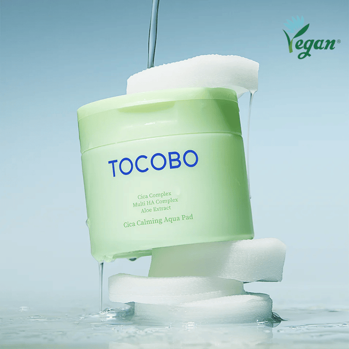 TOCOBO Cica Calming Aqua Pad aseteltuna toner padien väliin valuvan essencen kanssa. Vegaanisymboli korostaa tuotteen vegaanista koostumusta ja ihoystävällistä profiilia.