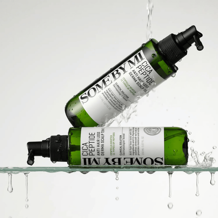 Två flaskor SOME BY MI Cica Peptide Anti Hair Loss Derma Scalp Tonic ligger i och ovanför vatten med droppar som skvätter, gröna flaskor med svart spraymunstycke och vit etikett.