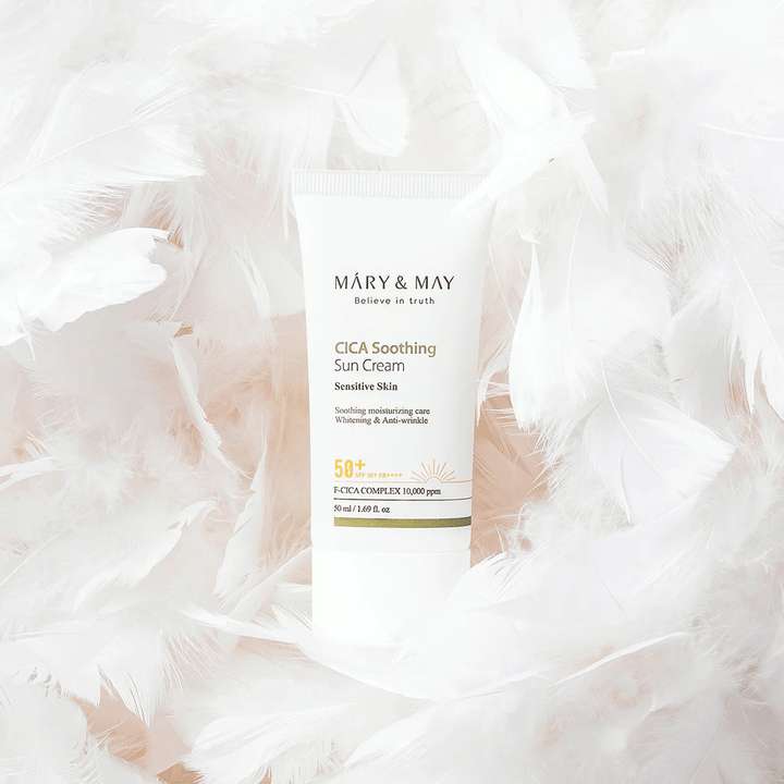 Mary&May CICA Soothing Sun Cream pehmeiden valkoisten höyhenten ympäröimänä. Kuva välittää hellävaraisuuden, mukavuuden ja kevyen koostumuksen tunteen, joka sopii herkälle iholle.