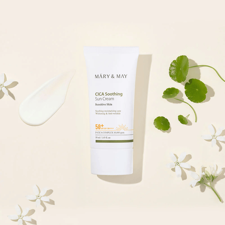Mary&May CICA Soothing Sun Cream SPF50+ PA++++ esiteltynä yhdessä voidemaisen koostumuksen, centella-lehtien ja valkoisten kukkien kanssa. Kuva tuo esiin tuotteen rauhoittavat ominaisuudet ja keskittymisen herkälle iholle.