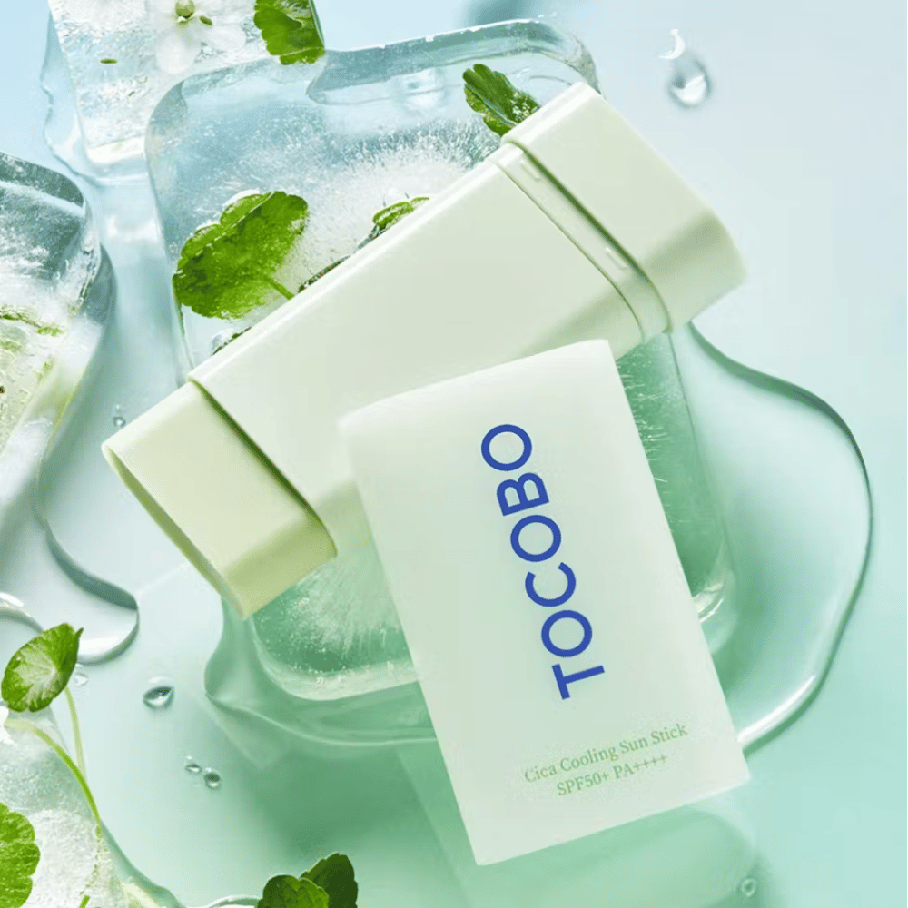 Tocobo Cica Cooling Sun Stick SPF50+ PA++++ jääpalojen päällä vihreiden kasvinlehtien kanssa, mikä välittää viilentävän ja virkistävän tunteen.