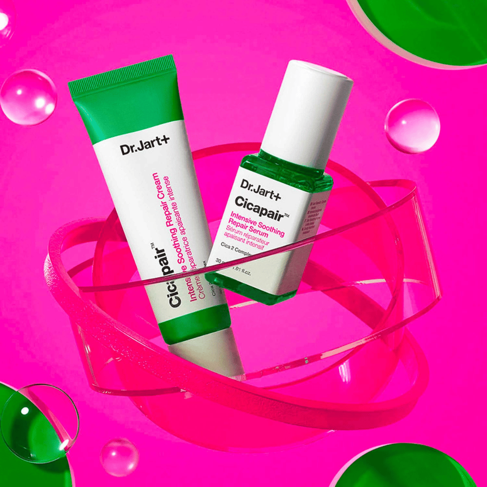 Dr.Jart+ Cicapair Intensive Soothing Repair Cream ja Serum vihreissä pakkauksissa, jotka seisovat vaaleanpunaisella pyöreällä alustalla. Tuotteet on suunniteltu rauhoittamaan ja korjaamaan ärtynyttä ihoa.