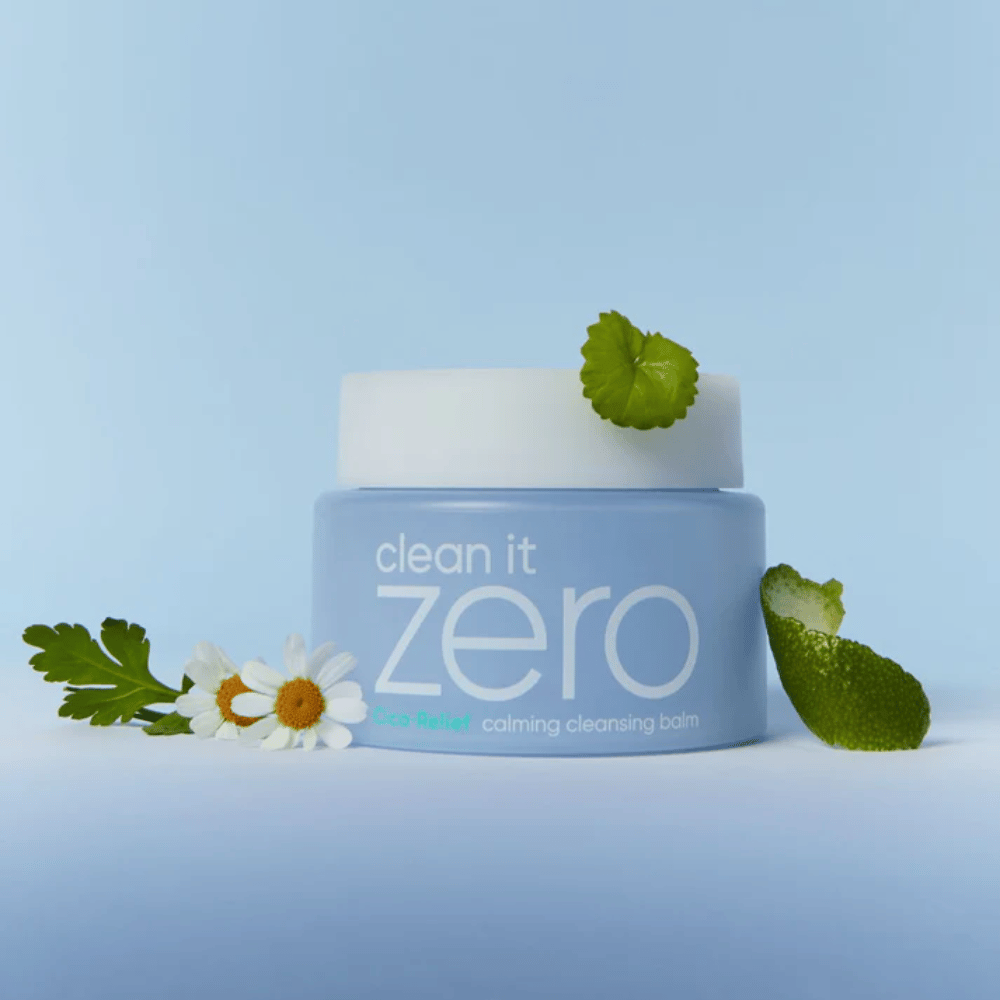 Clean It Zero Cica-Relief Calming Cleansing Balm sijoitettuna kasvien ja kukkien kanssa, kuvaa hellävaraista puhdistusta rauhoittavalla CICA:lla herkälle ja ärtyneelle iholle.