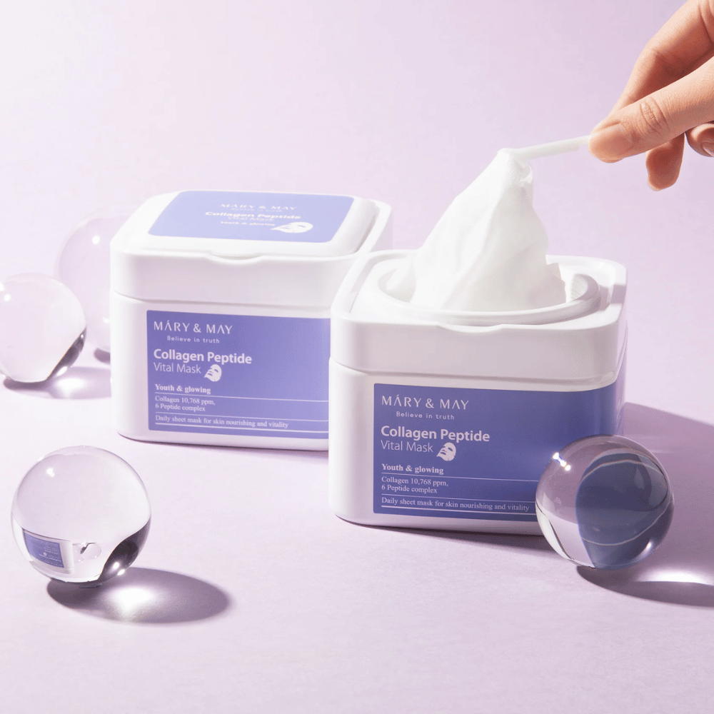 Käsi ottaa naamion MARY & MAY:n Collagen Peptide Vital Mask purkista. Naamio on tarkoitettu päivittäiseen käyttöön ravitsemaan ja heleyttämään ihoa, kollageenin ja peptidien tukemaan ihon nuorekkuutta.