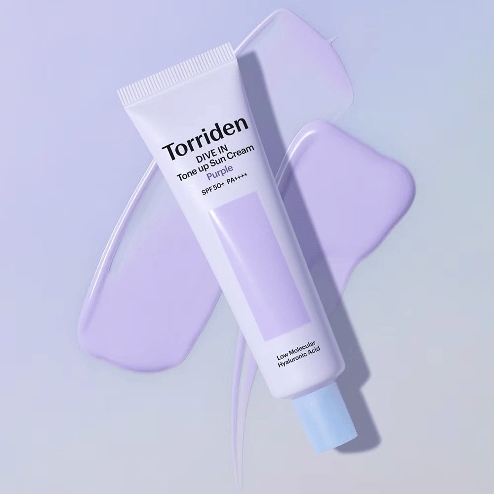 Torriden DIVE IN Tone Up Sun Cream Purple asetettuna levitetyn violetin voiteen päälle, mikä korostaa sävyä tasoittavaa ja hehkua antavaa vaikutusta.