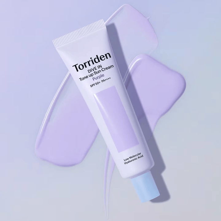 Torriden DIVE IN Tone Up Sun Cream Purple asetettuna levitetyn violetin voiteen päälle, mikä korostaa sävyä tasoittavaa ja hehkua antavaa vaikutusta.