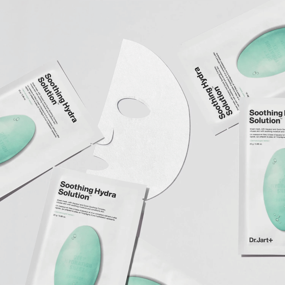 Useita "Soothing Hydra Solution" kasvonaamioiden pakkauksia Dr.Jart+ on levitetty vaalealle pinnalle. Keskelle on asetettu avattu naamio, joka näyttää sen valkoisen ja rei'itetyn rakenteen.