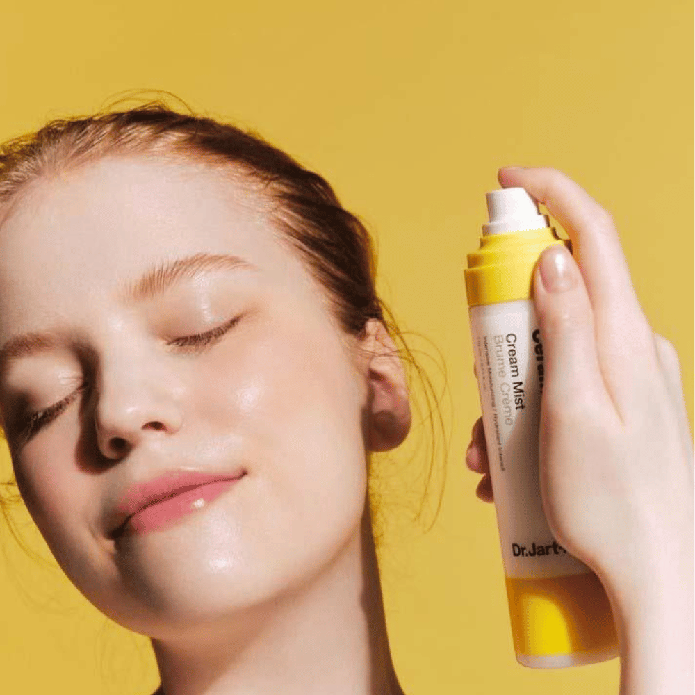 Nainen pitelee kasvoillaan Dr. Jart+ Ceramidin Cream Mist 110ml -pulloa, korostaen sen kosteuttavia etuja ja vegaanista koostumusta.