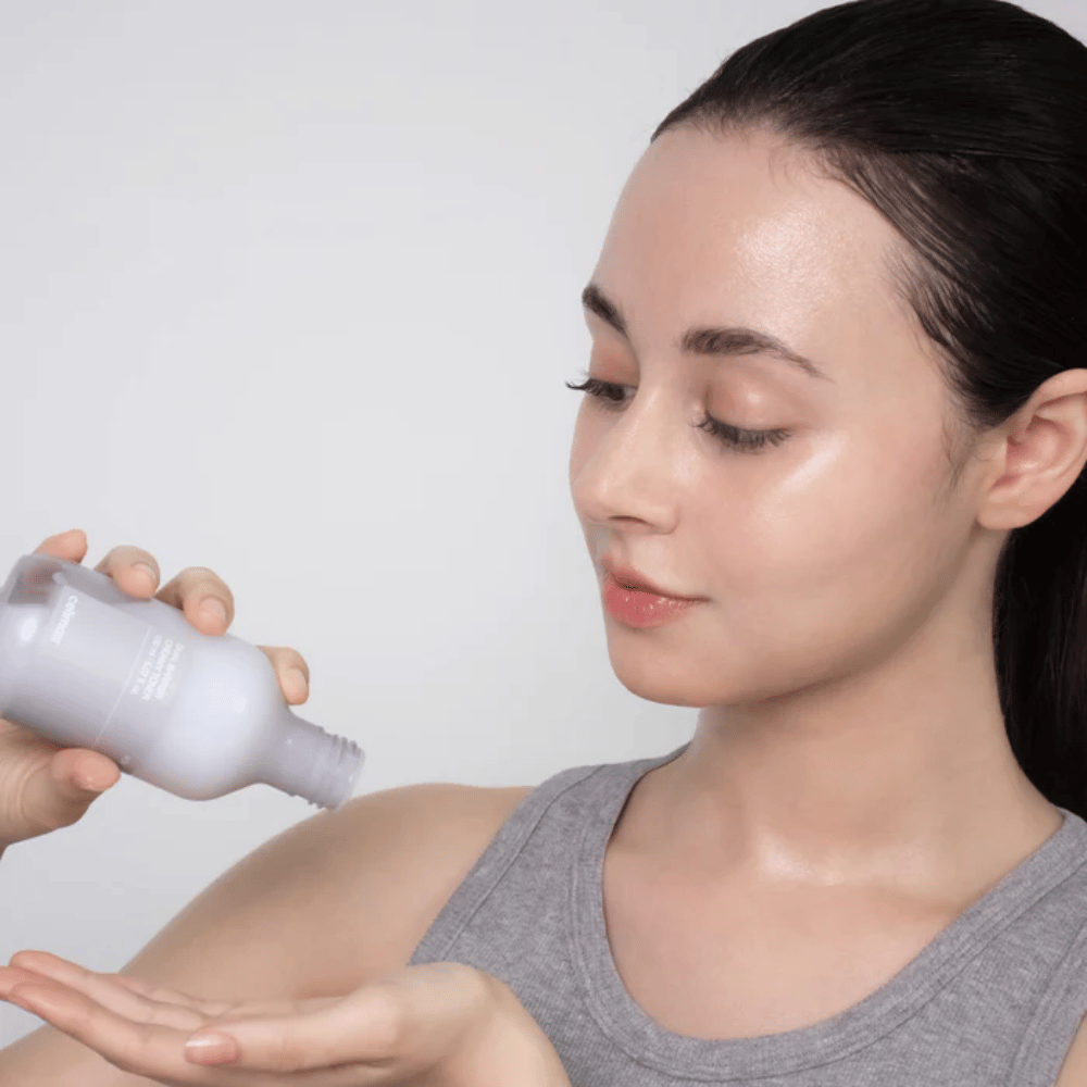 Nainen, jolla on kiiltävä, kosteutettu iho, levittää Celimax Dual Barrier Creamy Toner kaatamalla tuotteen kämmenelleen ennen ihonhoitorutiiniaan.