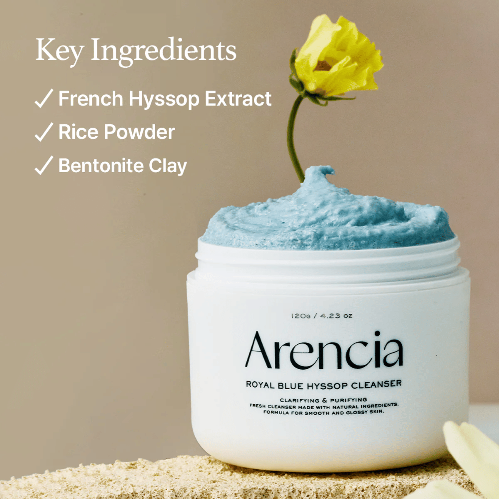 Kuva purkista "Arencia Royal Blue Hyssop Cleanser" täynnä sinistä puhdistusvoidetta. Keltainen kukka nousee voiteesta. Kuvan teksti korostaa kolmea avainainesosaa: French Hyssop Extract, Rice Powder ja Bentonite Clay.