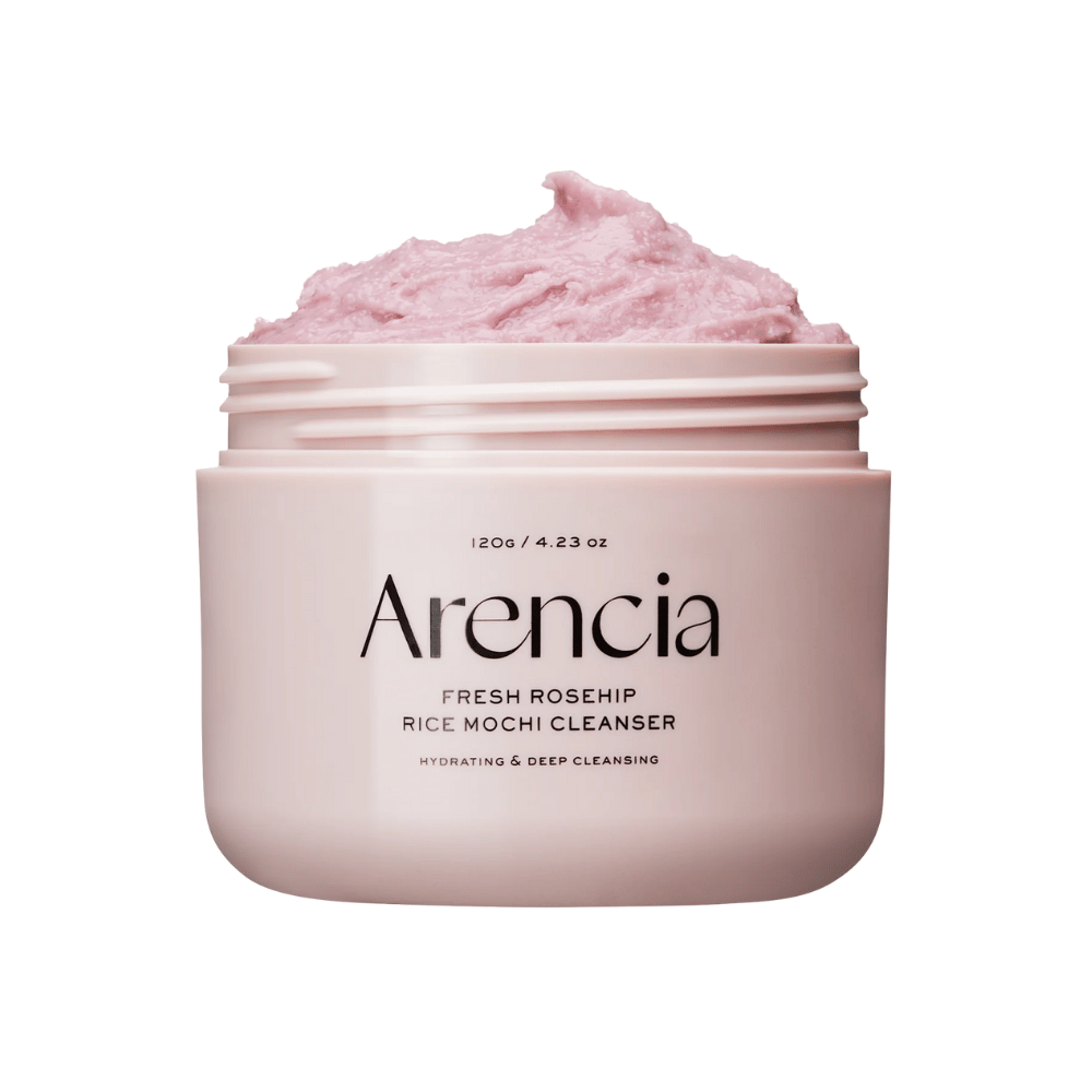 Lähikuva vaaleanpunaisesta purkista, jossa on Arencia Royal Rosehip Cleanser, täynnä vaaleanpunaista puhdistusvoidetta, jonka koostumus on vispattu ja mochia muistuttava. Purkin teksti osoittaa, että tuote kosteuttaa ja puhdistaa syvältä.