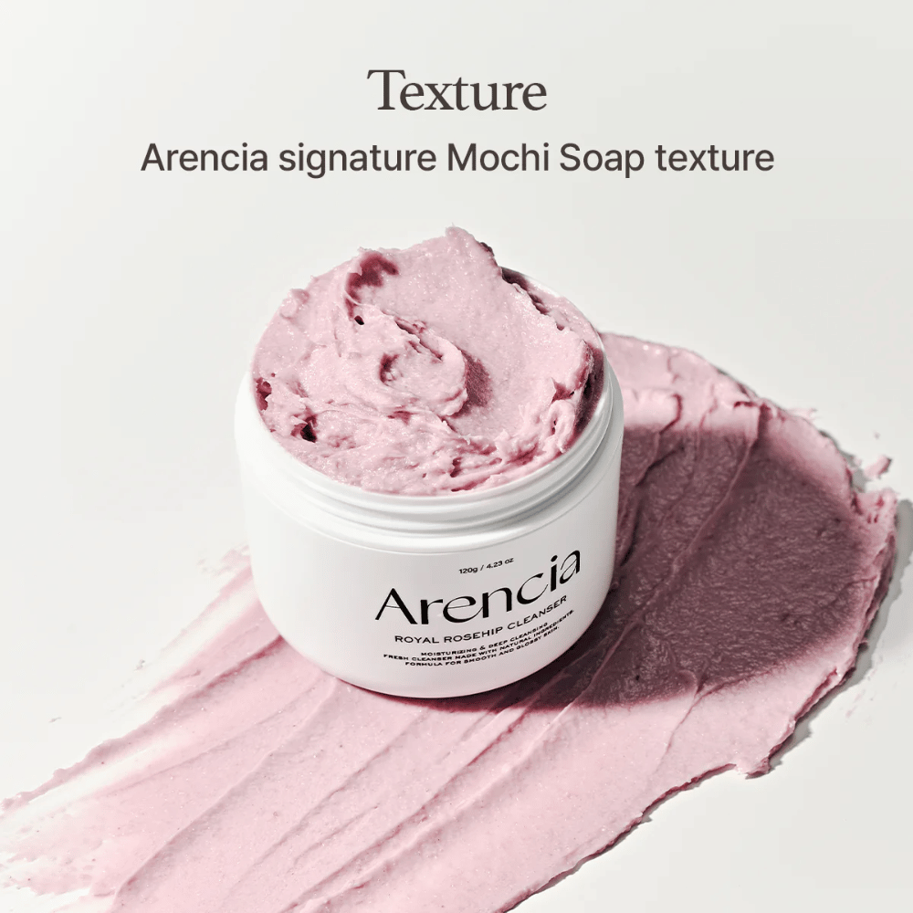 Purkki Arencia Royal Rosehip Cleanser näkyy vaaleanpunaisen, mochia muistuttavan puhdistusaineen päällä. Yläpuolella oleva teksti kuvailee tuotetta Arencian tunnusomaisena koostumuksena.