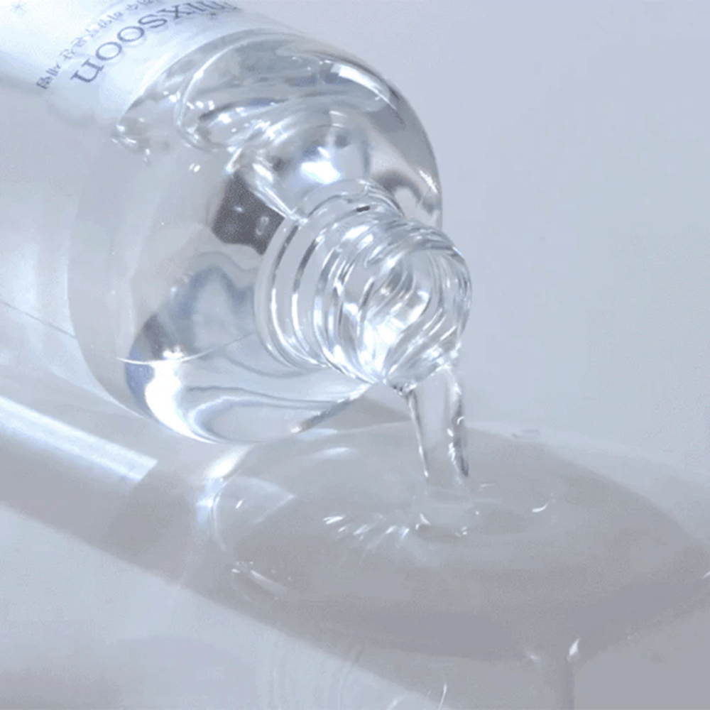 Lähikuva läpinäkyvästä seerumista, jota kaadetaan pullosta Mixsoon Glacier Water Hyaluronic Acid Serum kiiltävälle pinnalle.