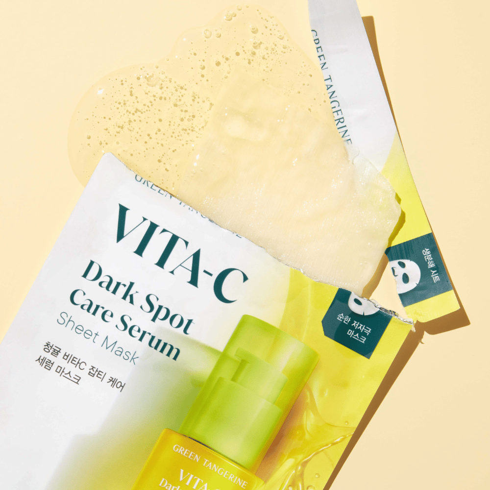 Avoin pakkaus VITA-C Dark Spot Care Serum Sheet mask:lle, jossa on kasvonaamio päällä ja vihreä seerumipullo, kaikki keltaista taustaa vasten.
