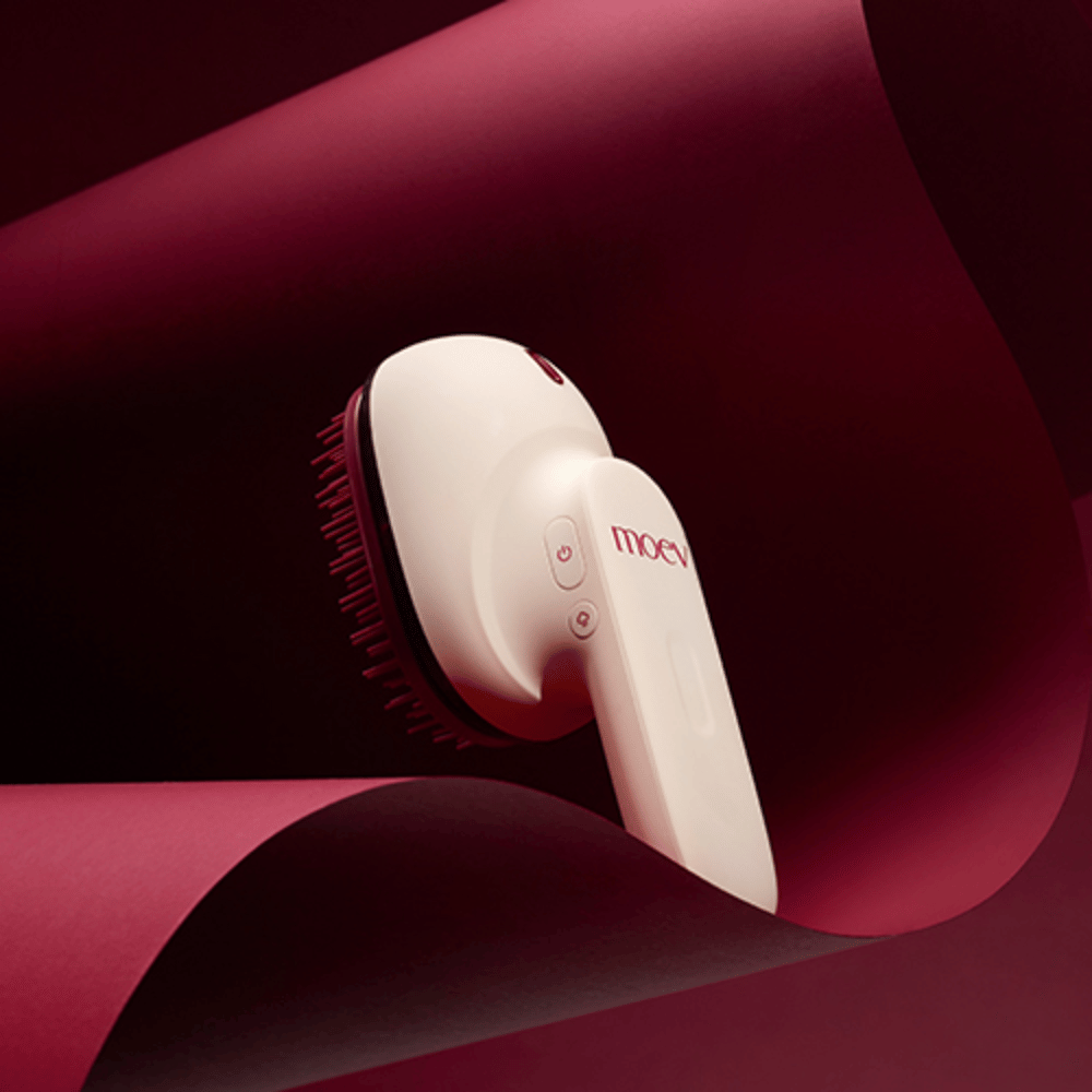 MOEV Hair Steamer Pro tyylikkäässä muotoilussa punaisella taustalla. Innovatiivinen hiustenhoitoharja, joka käyttää höyryä ja lämpöä antaakseen kiiltoa, pehmeyttä ja vahvistettua hiusterveyttä.