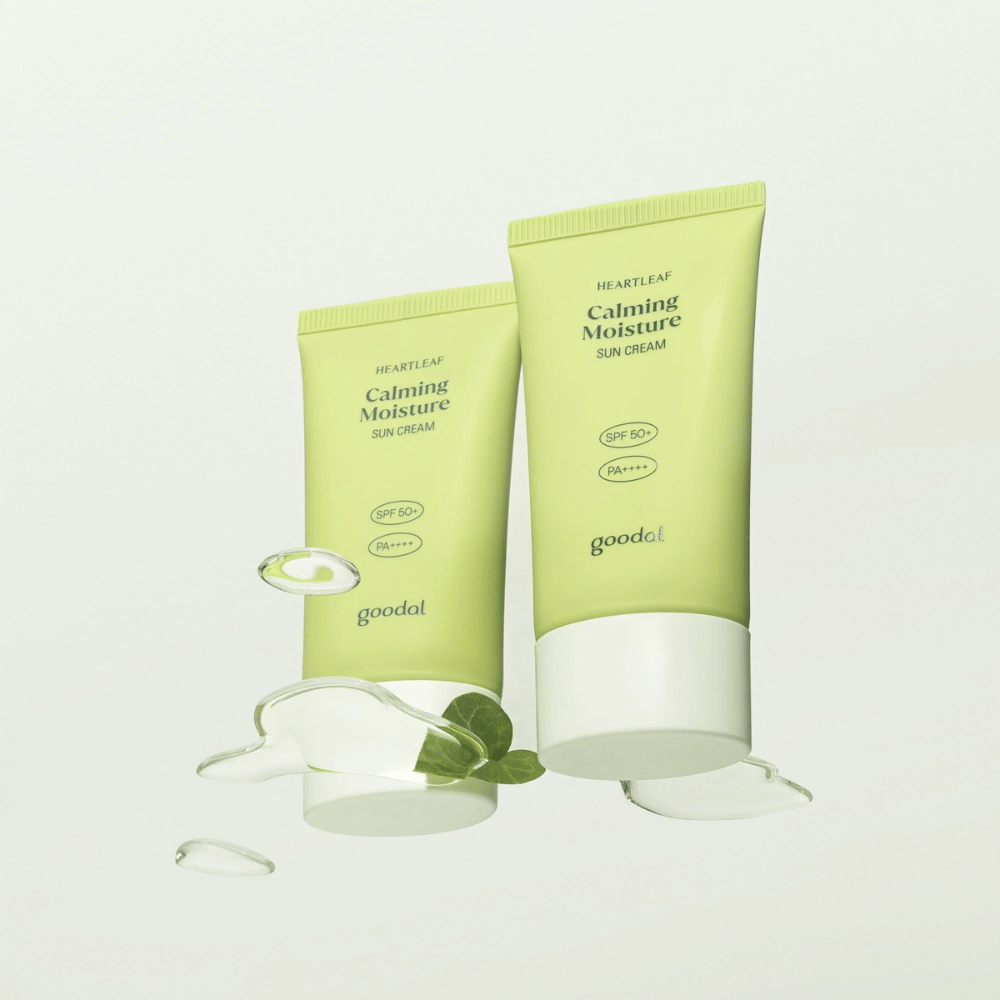 Kaksi tuubia Goodal Heartleaf Calming Moisture Sun Cream SPF50+ PA++++ ympäröitynä kasvinlehdillä ja seerumitipoilla vaaleaa taustaa vasten.