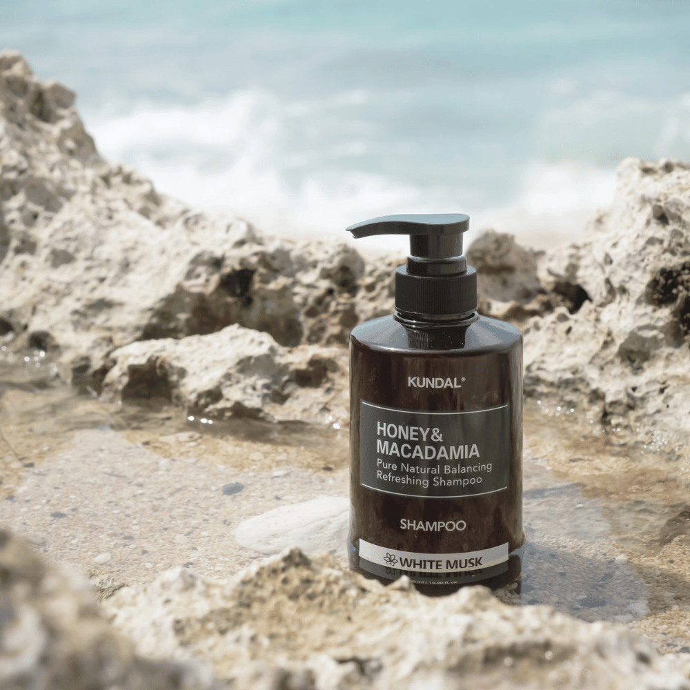 KUNDAL Honey & Macadamia Nature Shampoo White Musk sijoitettuna kallioille meren äärellä, luonnollinen hiustenhoitotuote, jossa raikas tuoksu.