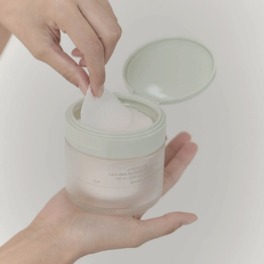 Käsi ottaa toner-tyynyn purkista Celimax Ji Woo Gae Cica BHA Blemish Toner Pad, täydellinen epäpuhtaalle iholle.
