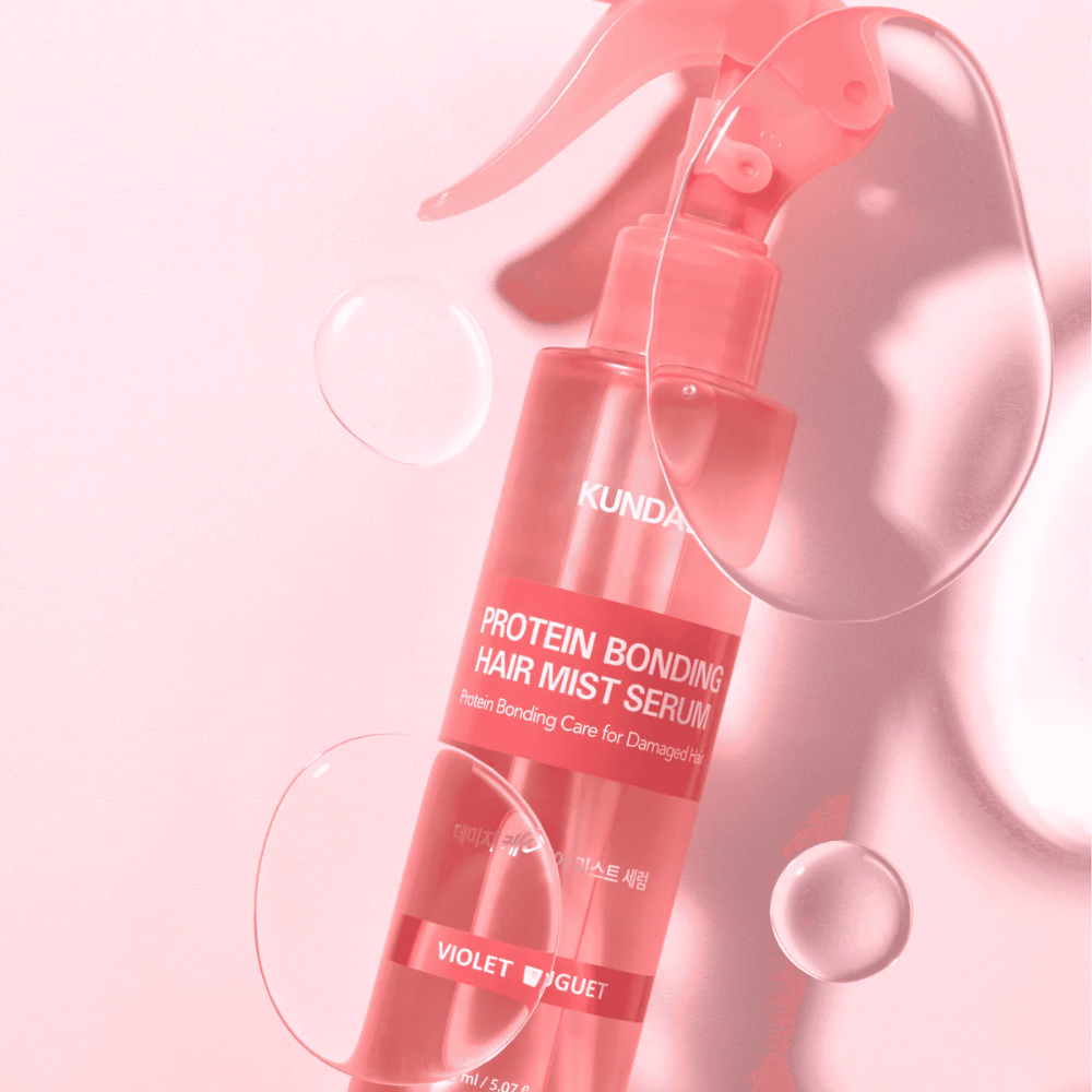 KUNDAL Protein Bonding Hair Mist Serum Violet Bouquet vaaleanpunaisessa suihkepullossa, kuvattuna vaaleanpunaista taustaa vasten vesipisaroilla.